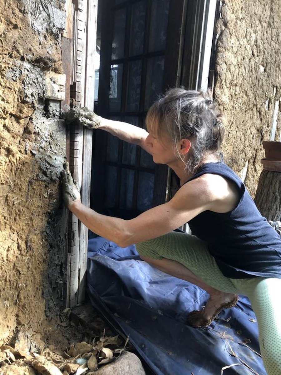 Shellie smooths handfuls of cob over the cob cottage.